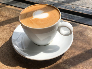 White coffee cup with heart latte art on wooden table