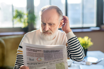 Grey-haired bearded man in reading a newspaper