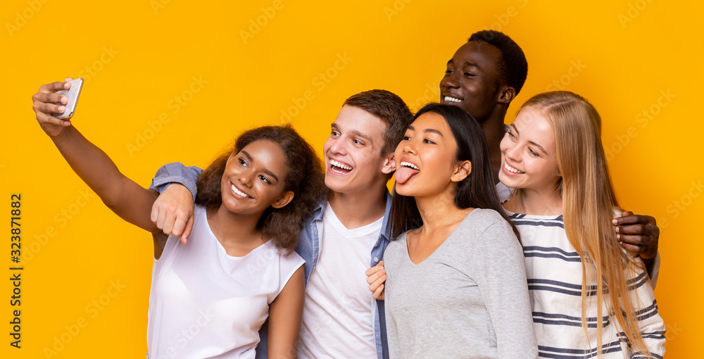 Wall mural Portrait of smiling friends taking group selfie over yellow background