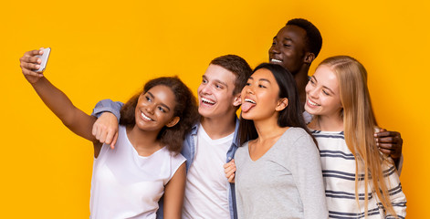 Portrait of smiling friends taking group selfie over yellow background