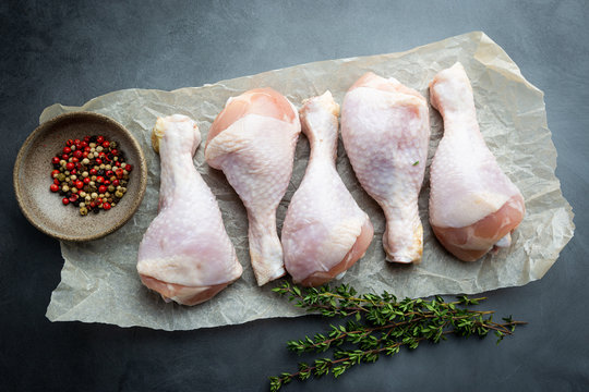 Raw chicken drumsticks on paper with herbs and seasonings on black background. Top view with copy space for your text.