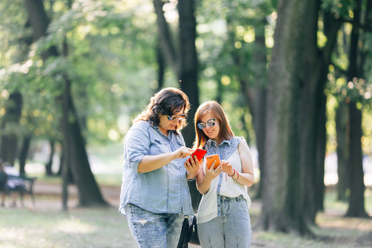 Two friends looking at pictures on a smartphone, girls with a smartphones talking in the park