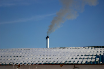 Modern steel chimney of a Russian sauna covered with snow against a blue sky.