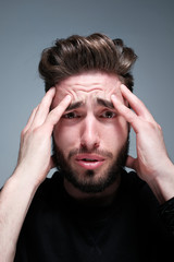 A young dark-haired man with a beard holds his head and shows different human emotions: hatred, fear, despair, horror, malaise, headache, clairvoyance. Close-up studio portrait of a man.