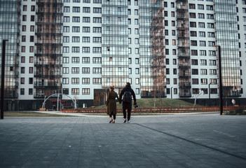 Back view of young beautiful couple in love walking outdoor in the city. Date, romantic, love concept.  View of urban apartment house, city landscape.