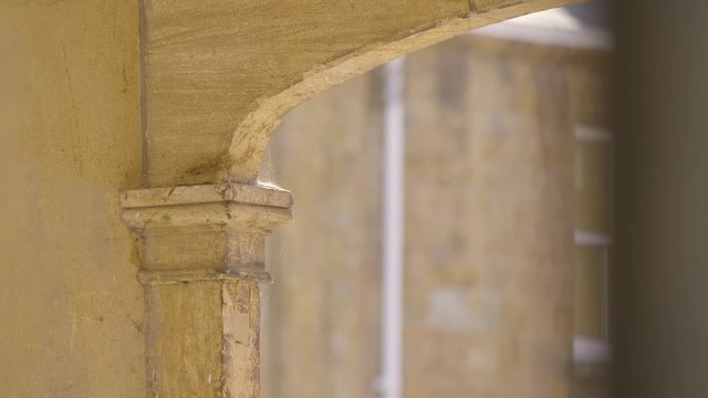 A daylight medium shot of a weathered concrete arch attached to a column's capital and painted in a yellowish colour.