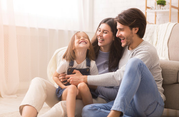 Playful Parents Tickling Their Little Daughter, Having Fun Together At Home