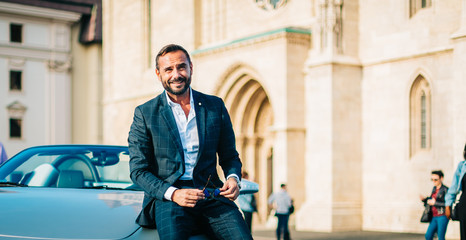 Successful happy businessman smiling on the street next to convertible car