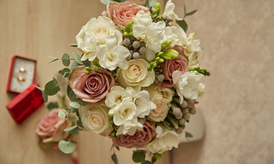 Wedding rings and beautiful wedding bouquet on natural wooden desk with nature in background.