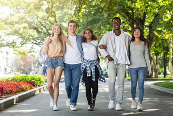 Carefree international students walking together in public park after studying