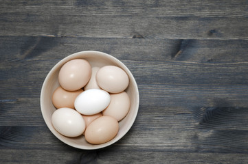 Chicken eggs in a light wooden bowl on a dark wooden table. Background. The concept of healthy farm egg production