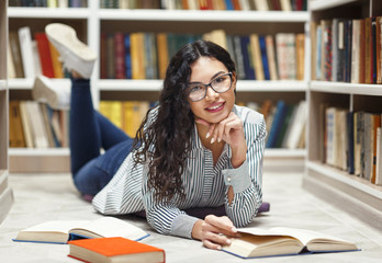 Smiling latina girl reading books lying at library