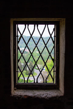Vertical picture of the view of the green trees of the mountain of Loket, in Czech Republic, through the grills of a window from Loket Castle