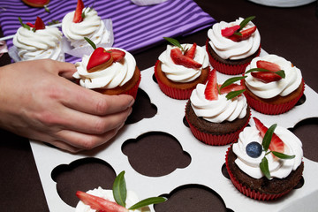 assorted cupcakes, hand forward one cupcake, cream and strawberries