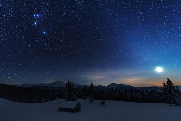 A bright starry night in the mountains with the Milky Way in the sky, Venus and millions of stars highlighting beautiful mountain huts in the valley.