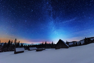 A bright starry night in the mountains with the Milky Way in the sky, Venus and millions of stars highlighting beautiful mountain huts in the valley.