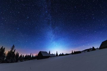 A bright starry night in the mountains with the Milky Way in the sky, Venus and millions of stars highlighting beautiful mountain huts in the valley.