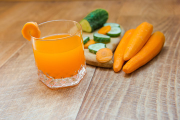 Carrot juice. Healthy food, healthy drink. Orange juice in a glass and next to peeled carrots, sliced cucumber.  healthy eating for breakfast. Wood background