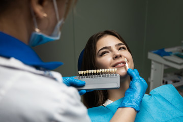 dentist in blue medical gloves and mask applying sample from tooth enamel scale to woman patient teeth to choose right shade for bleaching procedure