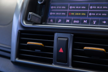 Close up emergency light button in a red car The side has a yellow air conditioner adjustment. On the top is a car radio screen that is on for music and news from radio programs.