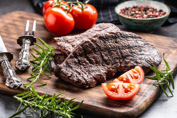 Two beef rump steaks with herbs tomatoes salt and spices on butcher board