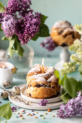 Traditional cupcake Easter cake kraffin with raisins and icing sugar on the table. Easter cakes, candles and a bouquet of lilac flowers.