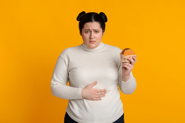 Stomachache. Girl Holding Burger And Touching Stomach Feeling Bad After Eating Junk Food Standing...