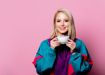 Blonde woman in 90s sport suit with cup of coffee on pink background