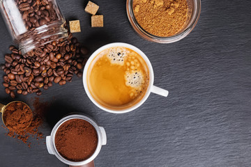 A cup of black coffee, filter holder of espresso maker and scattered roasted coffee beans
