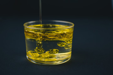 Olive oil falling on water in a low glass with drops of oil on the bottom. Isolated on a black background.                          Abstract concept. Copy space 