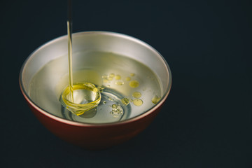 Olive oil falling on water, with drops of oil on the water, in a red and silver bowl .Abstract concept,can't be mixed.Copy space