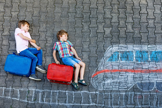 Two little kids boys having fun with train picture drawing with colorful chalks on asphalt. Children having fun with chalk and crayon painting. going on vacations and travel. Friends with suitcases