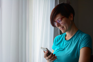 Side view of joyful Woman holding digital gadget and looking at its screen. Girl shopping online, blogging, checking email, chatting.