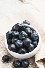 Fresh heap of blueberry in white clean bowl on sack cloth.