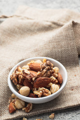 Mixed nuts in white clean bowl on sack cloth. Healthy food and snack concept.