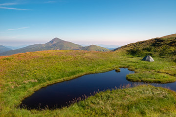 Fototapeta premium A mountain lake near which a tourist tent is set against the backdrop of the Hoverla mountain. Mountain landscape.