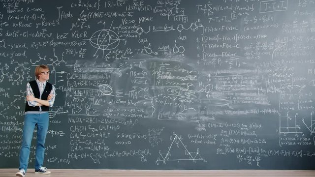 Time-lapse of smart young man scientist walking in class looking at chalkboard with formulas thinking about science problem. People and challenges concept.