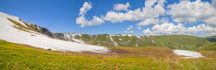 Fototapeta premium Spring in the mountains. Snow on the slopes, green meadows. Panoramic view. 