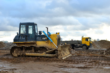 Obraz premium Track-type bulldozer during of large construction jobs at building site. Land clearing, grading, pool excavation, utility trenching, utility trenching and foundation digging. Earth-moving equipment.