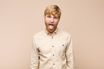 young blonde man feeling disgusted and irritated, sticking tongue out, disliking something nasty...
