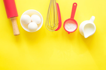 Ingredients and devices for baking. Flour, eggs, milk, rolling pin, whisk on a yellow background, copy space, top view,flat lay.