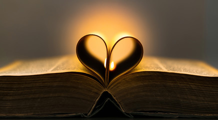 Old book pages in a heart shape with a flame in the background  - 323892234
