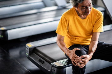 Elderly man having pain in his knee at the gym