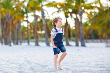 Adorable active little kid boy having fun on tropical beach of island. Happy cute child relaxing, playing, enjoying, running and jumping on sunny warm day near palms and ocean. Active family vacations