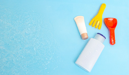 Sunscreen cream spf lotion to remedy kids skin from sun with colorful water toys on blue water surface of pool, top view. Concept ultraviolet protection product, summer children cosmetics.