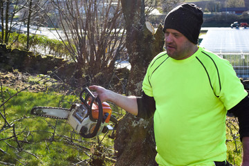 Obraz premium Worker in the garden with a chainsaw. Concept: spring garden work.
