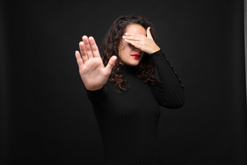 young pretty woman covering face with hand and putting other hand up front to stop camera, refusing...