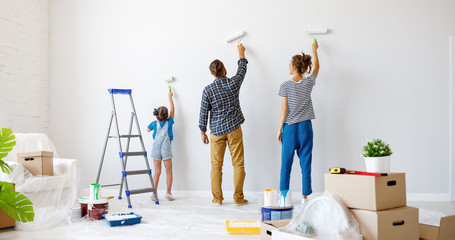 Repair in apartment. Happy family mother, father and child daughter  paints wall .