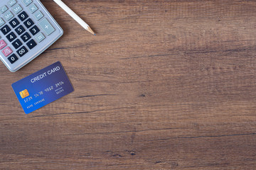 Top view of a blue credit card, pencil and calculator on wooden table. Space for text. Wood texture...