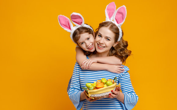 Happy easter! family mother and child daughter with ears hare getting ready for holiday on colored yellow background.
